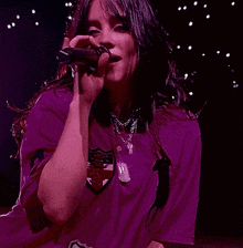 billie eilish is singing into a microphone while wearing a purple shirt with the number 2 on it