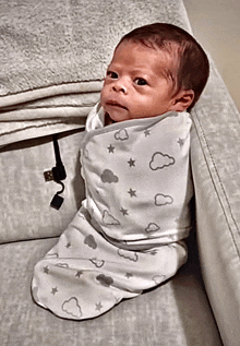 a baby is wrapped in a white blanket with clouds and stars on it