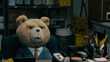 a teddy bear in a suit sits at a desk