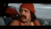 a man wearing a red beanie and a red tank top with chains around his neck