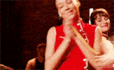 a woman in a red dress is clapping her hands in front of a brick wall .