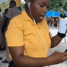 a woman in a yellow shirt is listening to music on her phone .