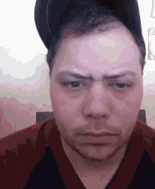 a man wearing a baseball cap and a red shirt is making a funny face .