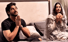 a man and a woman sit on a bed praying