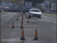 a white car is driving through a row of orange traffic cones with motorweek.org written on the bottom right