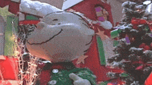 a stuffed snoopy is standing in front of a christmas tree and gifts .