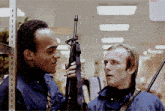 two men are standing next to each other one holding a gun