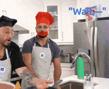 two men wearing chef hats and aprons are cooking in a kitchen with the words " wait " in blue