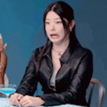 a woman in a black leather jacket is sitting at a table with a glass of water .