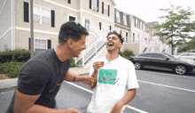 two men are laughing in a parking lot and one of them is wearing a shirt that says " i love you "