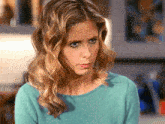 a woman with blonde hair wearing a blue sweater looks at the camera