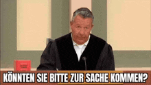 a man in a judge 's robe is sitting in front of a microphone in a courtroom and talking into it .
