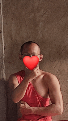 a man in a red tank top holds a red heart in front of his face