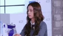 a woman in a school uniform is sitting at a desk holding a box .