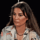 a woman wearing a floral shirt and a necklace with the letter t on it