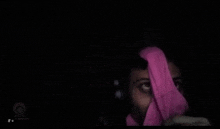 a woman is hiding her face with a pink scarf in the dark .