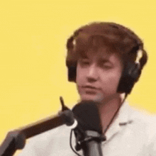 a man wearing headphones is standing in front of a microphone and smiling .