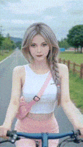 a woman in a white crop top and pink pants is riding a bike down a road .