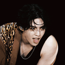 a man wearing a leopard print jacket and a black tank top sticking his tongue out