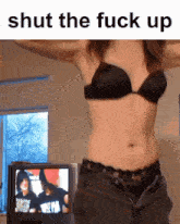 a woman in a black bra is standing in front of a television with the words shut the fuck up written above her