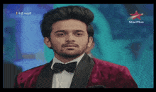 a man in a red jacket and black bow tie is on a star plus channel