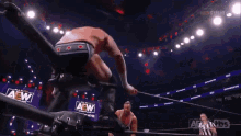 a wrestler is jumping over another wrestler while a referee looks on