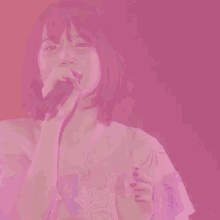 a woman singing into a microphone in a pink background
