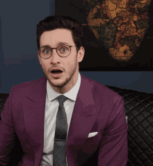 a man wearing a purple suit and tie is sitting on a couch