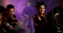 a group of people are dancing and singing in front of a man playing a guitar and a woman singing into a microphone