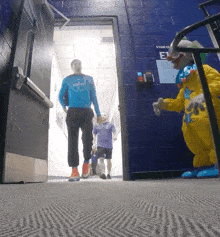 a man in a blue shirt that says ' i 'm a monster ' on it walks through a hallway