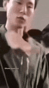 a man in a green jacket is making a funny face while holding his hand to his face .
