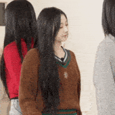 a woman with long black hair is wearing a brown sweater with a letter r on the front