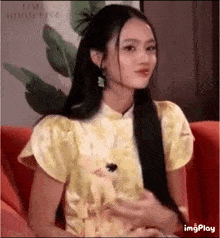 a woman with long black hair is sitting on a couch wearing a yellow dress and earrings .