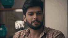 a man with a beard wearing a plaid shirt is looking at the camera
