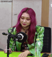 a woman with pink hair is sitting in front of a microphone with a bottle of water next to her
