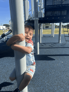 a young boy climbs up a pole at a playground
