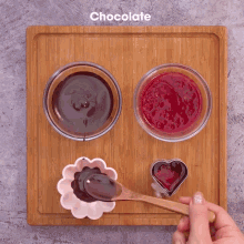 a wooden cutting board with bowls of chocolate and raspberry jam on it