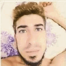 a shirtless man with a beard is laying on a bed and taking a selfie .