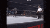 a referee is standing in the middle of a wrestling ring watching a wrestler .