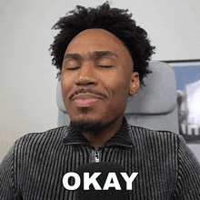a man with his eyes closed is wearing a sweater that says okay on it