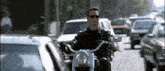 a man wearing sunglasses is riding a motorcycle on a busy street