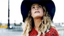 a woman wearing a black hat and a red sweater is looking up at the sky .