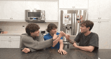 three young men are sitting at a table in front of a refrigerator that says lg on it