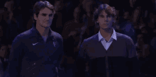 two men are standing next to each other in front of a crowd . one of the men is wearing a nike jacket .