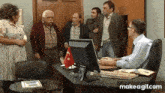 a group of people are standing around a man sitting at a desk in front of a computer ..