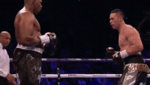 two men are fighting in a boxing ring with a referee in the background .