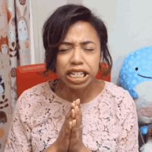 a woman in a pink lace top is praying with her hands folded