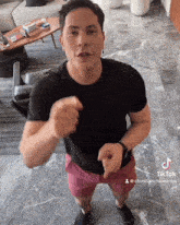 a man wearing a black shirt and pink shorts is pointing at the camera