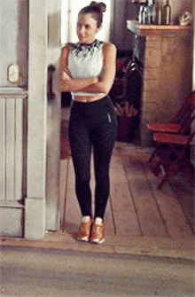 a woman in a white crop top and black leggings stands with her arms crossed