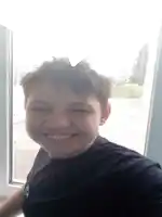 a young boy taking a selfie in front of a window with his eyes closed